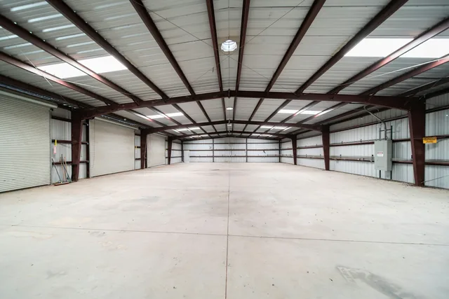 Empty warehouse interior with exposed steel roof beams, rooflights and a concrete floor.